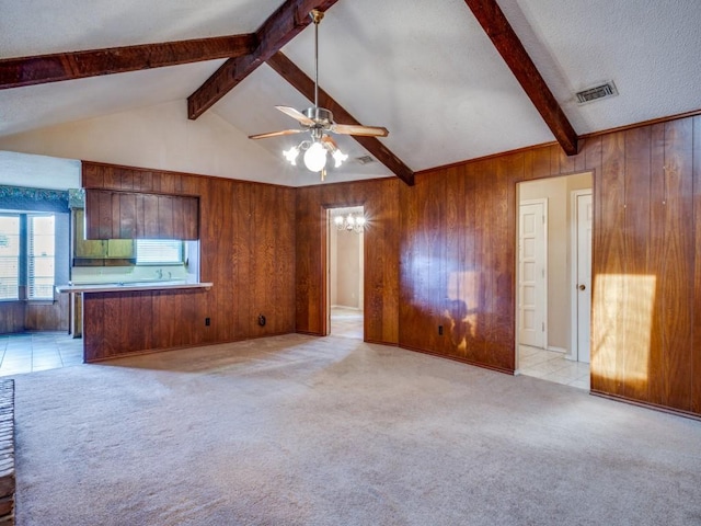 unfurnished living room with a textured ceiling, light colored carpet, ceiling fan, lofted ceiling with beams, and wood walls