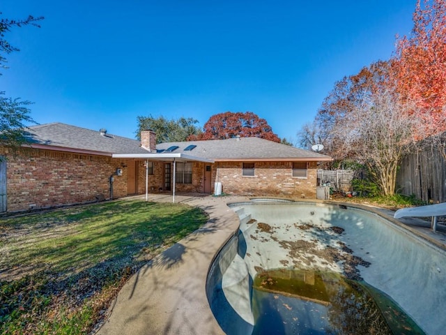 rear view of property with a patio area, a yard, and an empty pool