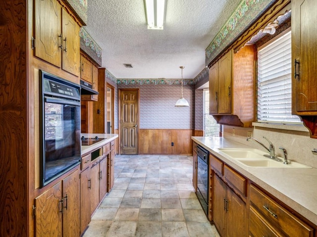 kitchen featuring sink, wood walls, a textured ceiling, decorative light fixtures, and black appliances