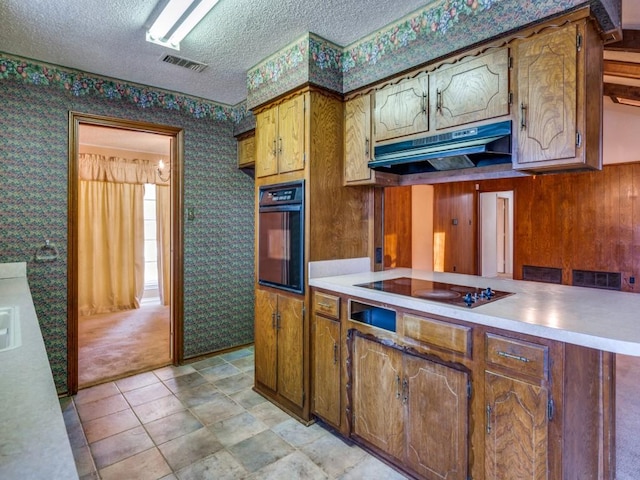 kitchen with a textured ceiling, light colored carpet, wooden walls, and black appliances