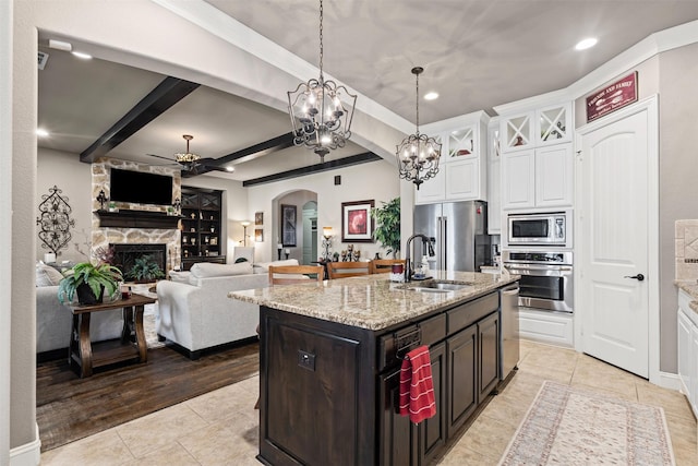 kitchen with a stone fireplace, white cabinets, dark brown cabinets, sink, and stainless steel appliances