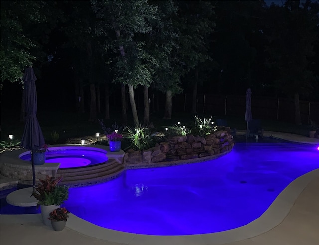 pool at twilight featuring an in ground hot tub