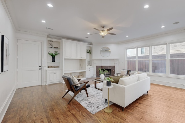 living room featuring a fireplace, ceiling fan, light wood-type flooring, and crown molding