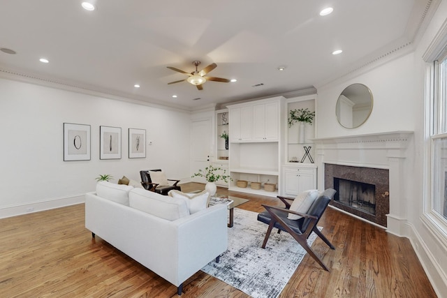 living room with crown molding, ceiling fan, a premium fireplace, and light wood-type flooring