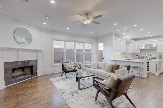 living room with ceiling fan, crown molding, sink, light hardwood / wood-style floors, and a tiled fireplace