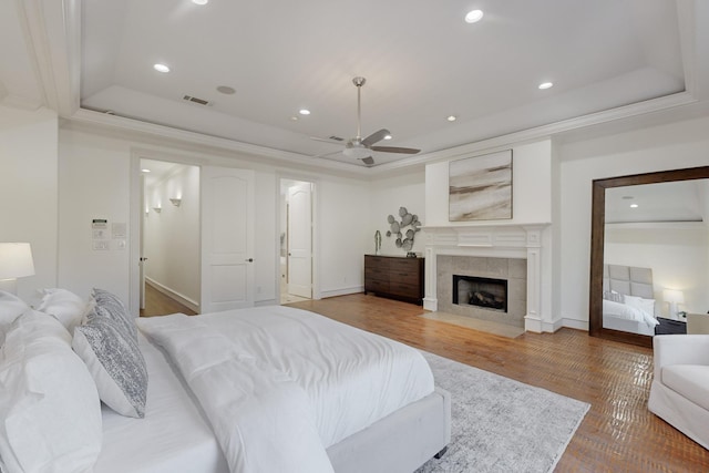 bedroom with a raised ceiling, ceiling fan, a fireplace, and wood-type flooring