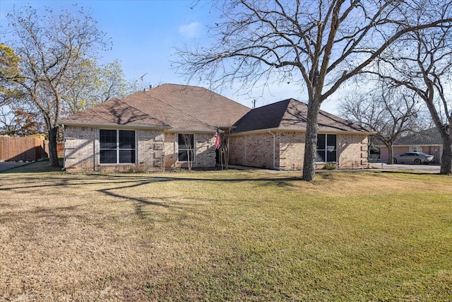 view of front of home with a shingled roof, fence, a front lawn, and brick siding