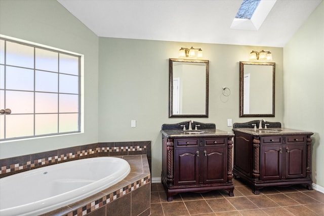 full bathroom featuring two vanities, vaulted ceiling with skylight, a garden tub, and a sink