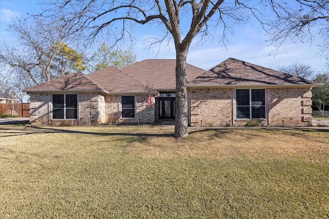 view of front of property with roof with shingles, a front lawn, and brick siding