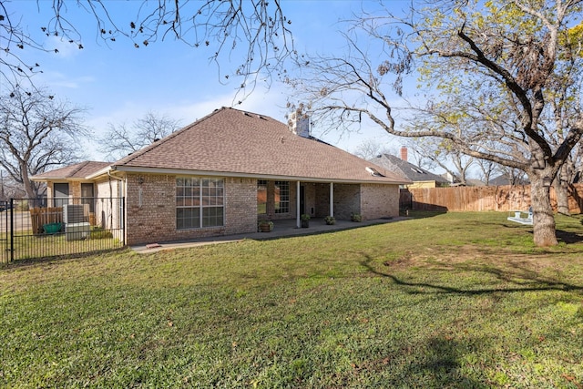 back of property with brick siding, a chimney, a shingled roof, a lawn, and fence