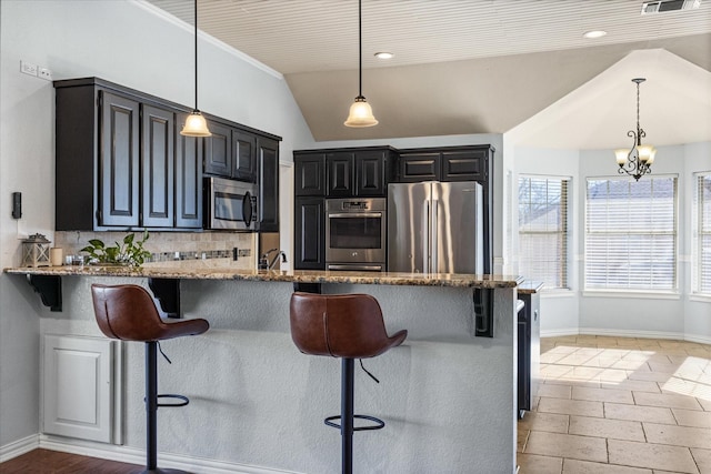 kitchen with a kitchen bar, appliances with stainless steel finishes, light stone countertops, and hanging light fixtures