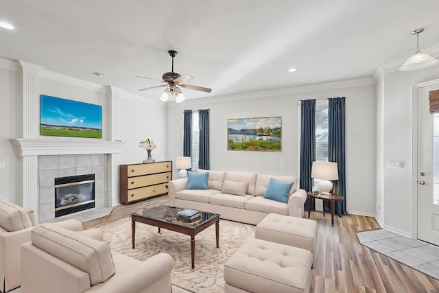 living room featuring a tile fireplace, light wood-type flooring, ceiling fan, and crown molding