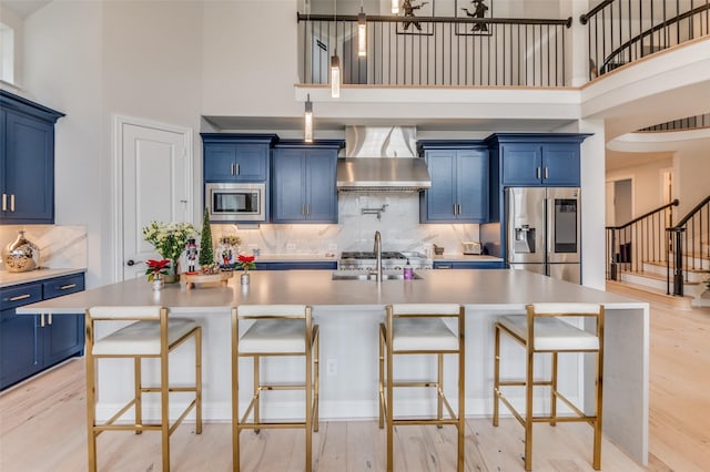 kitchen with blue cabinets, appliances with stainless steel finishes, a breakfast bar area, and wall chimney range hood