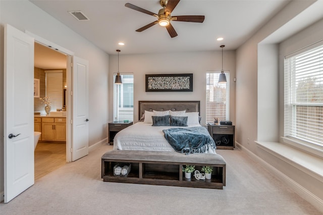 bedroom with ceiling fan, light colored carpet, ensuite bathroom, and multiple windows