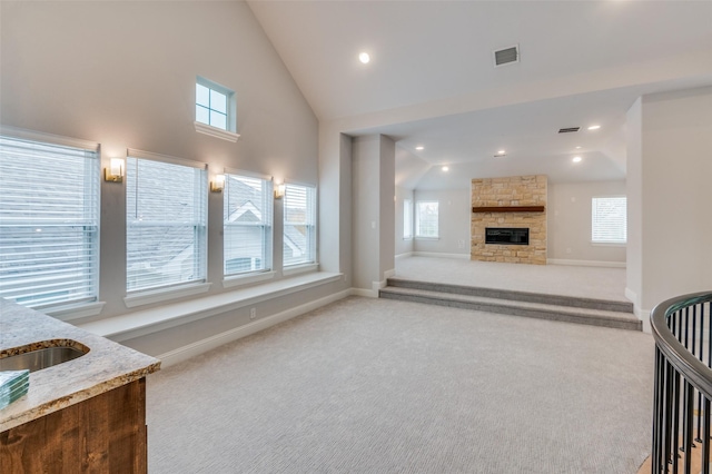 living room with high vaulted ceiling, a stone fireplace, light colored carpet, and sink