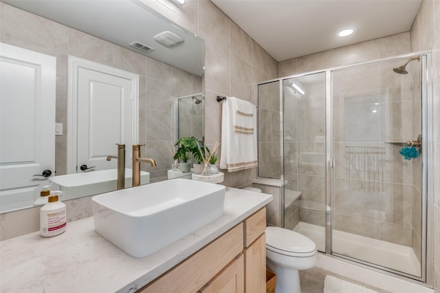 bathroom with vanity, toilet, tile walls, and walk in shower