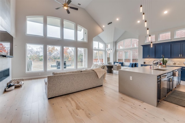 interior space featuring a tile fireplace, high vaulted ceiling, sink, ceiling fan, and light hardwood / wood-style flooring