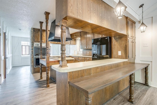 kitchen featuring pendant lighting, appliances with stainless steel finishes, island range hood, kitchen peninsula, and light wood-type flooring