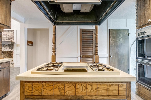 kitchen featuring white gas stovetop, a kitchen island, extractor fan, and light hardwood / wood-style flooring