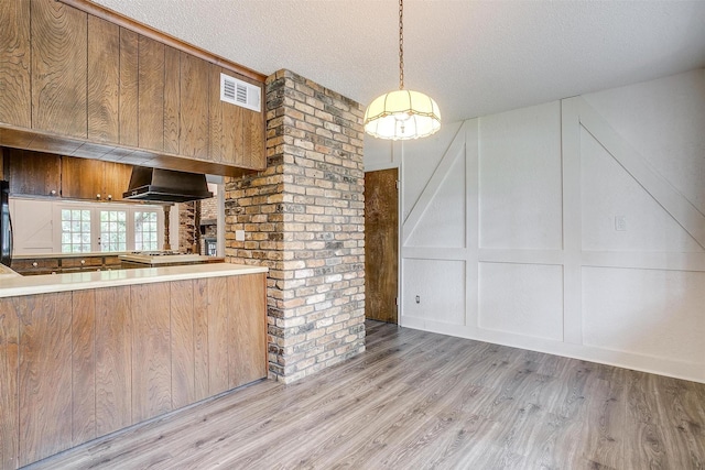 kitchen with wall chimney exhaust hood, a textured ceiling, light wood-type flooring, kitchen peninsula, and pendant lighting