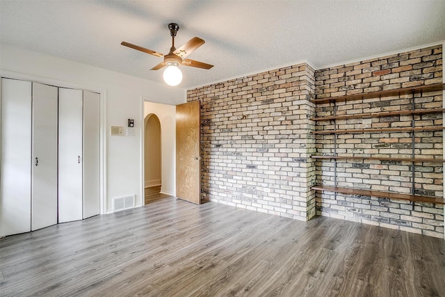 unfurnished bedroom with ceiling fan, hardwood / wood-style floors, a textured ceiling, brick wall, and a closet