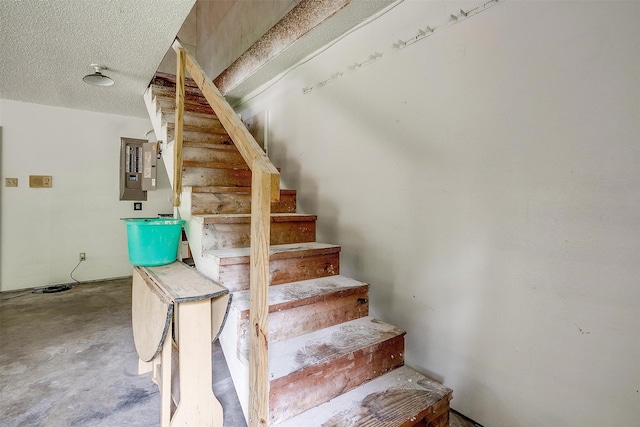 stairway featuring electric panel, concrete floors, and a textured ceiling