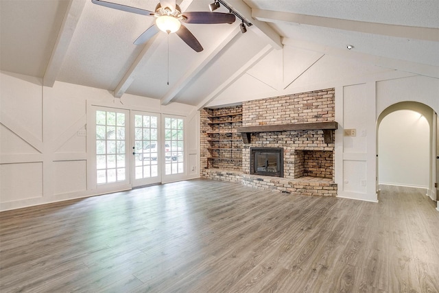 unfurnished living room with built in shelves, wood-type flooring, lofted ceiling with beams, a textured ceiling, and a fireplace