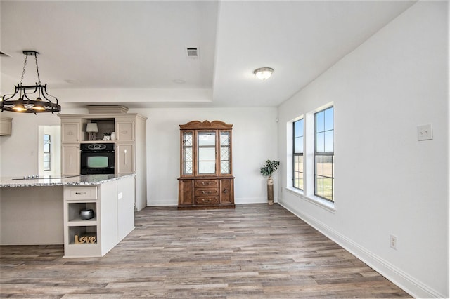 kitchen with hanging light fixtures, wood-type flooring, light stone countertops, white cabinets, and oven