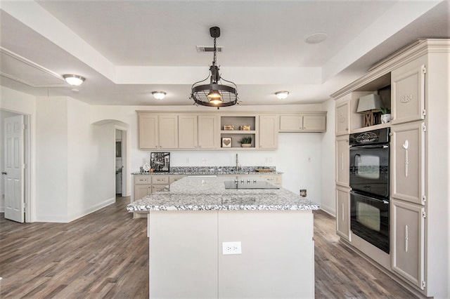 kitchen featuring pendant lighting, double oven, a center island, light stone counters, and a tray ceiling