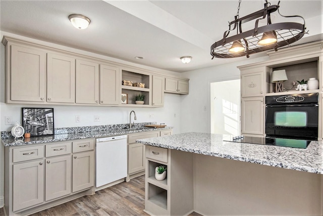 kitchen featuring light stone countertops, black appliances, decorative light fixtures, cream cabinetry, and light wood-type flooring