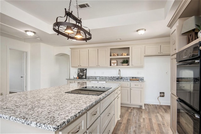 kitchen with a center island, a tray ceiling, black appliances, light hardwood / wood-style floors, and decorative light fixtures