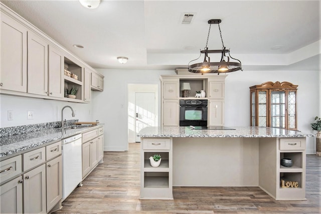 kitchen with sink, hanging light fixtures, light stone counters, black appliances, and a kitchen island