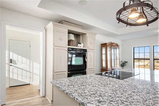 kitchen featuring light stone counters, light hardwood / wood-style floors, black appliances, and a raised ceiling