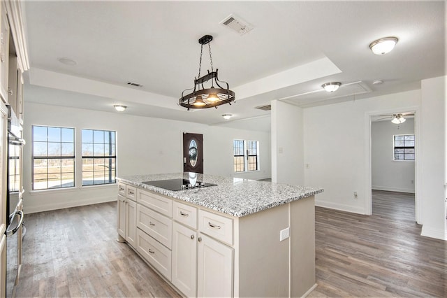 kitchen with white cabinetry, light stone counters, a center island, a tray ceiling, and black electric stovetop