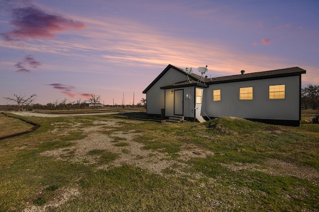 back house at dusk featuring a lawn