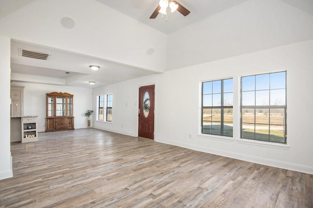 unfurnished living room with ceiling fan, a raised ceiling, and light wood-type flooring