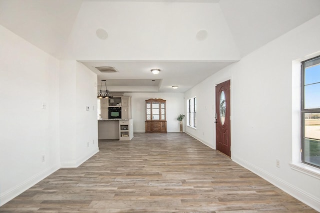 hall with lofted ceiling, a healthy amount of sunlight, and light wood-type flooring