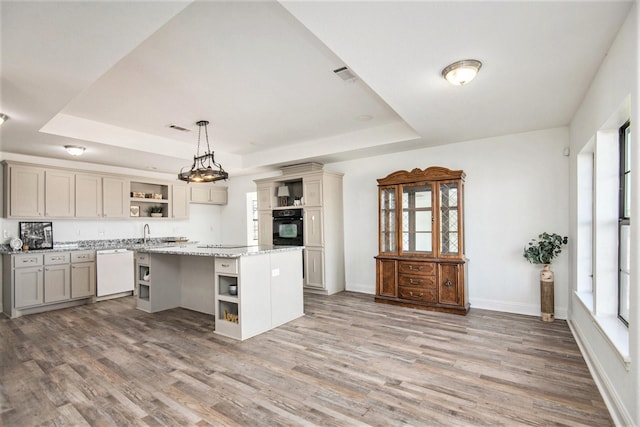 kitchen with light stone counters, a center island, a raised ceiling, pendant lighting, and black appliances