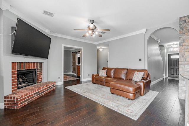 living room featuring ceiling fan, crown molding, dark wood-type flooring, and a brick fireplace