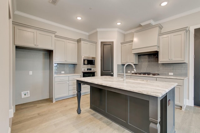 kitchen with light stone countertops, premium range hood, appliances with stainless steel finishes, and light wood-type flooring