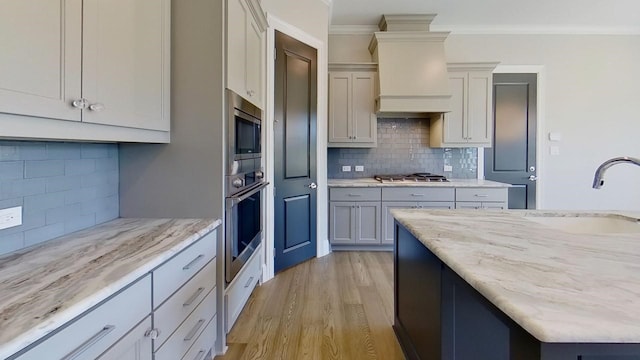 kitchen with sink, custom exhaust hood, crown molding, light wood-type flooring, and stainless steel appliances