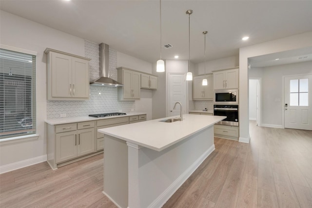 kitchen with light wood-type flooring, stainless steel appliances, wall chimney exhaust hood, and sink