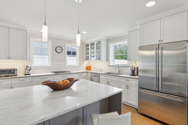 kitchen with appliances with stainless steel finishes, sink, white cabinets, hanging light fixtures, and light stone counters