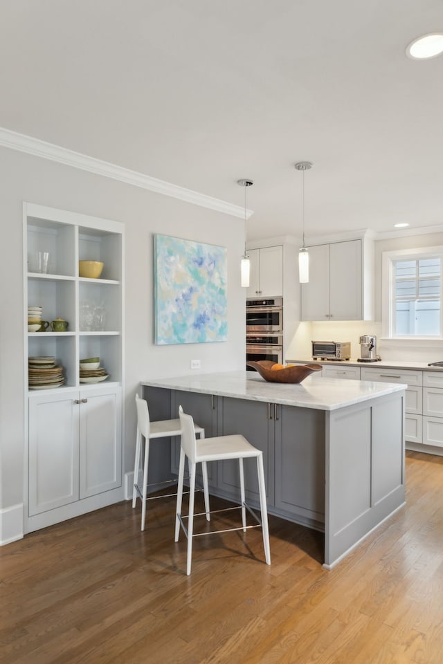 kitchen featuring pendant lighting, a breakfast bar, white cabinetry, double oven, and light hardwood / wood-style floors