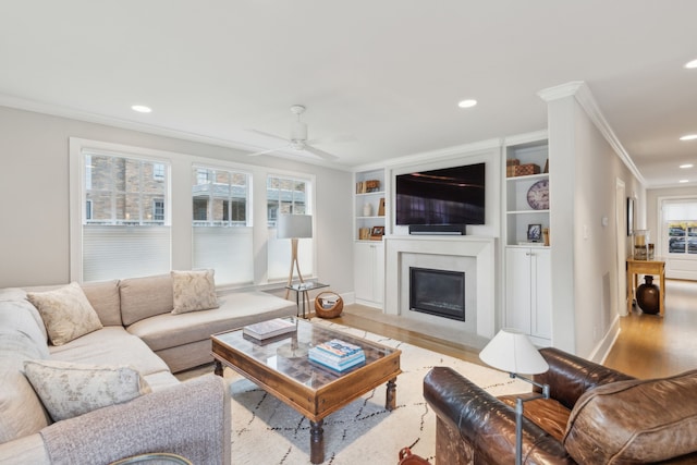 living room featuring ornamental molding, ceiling fan, light wood-type flooring, and built in shelves