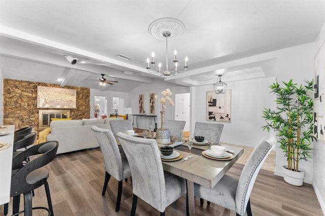 dining room with beam ceiling, a fireplace, wood-type flooring, and ceiling fan with notable chandelier