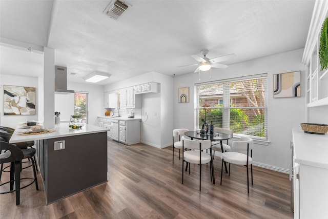 kitchen featuring ceiling fan, dishwasher, dark hardwood / wood-style flooring, a kitchen bar, and white cabinets