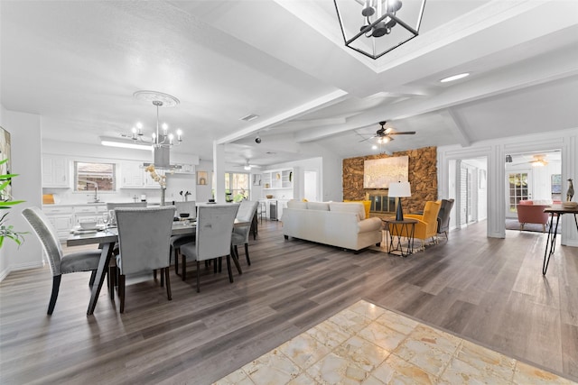 dining area featuring vaulted ceiling with beams, a chandelier, a stone fireplace, and light hardwood / wood-style flooring