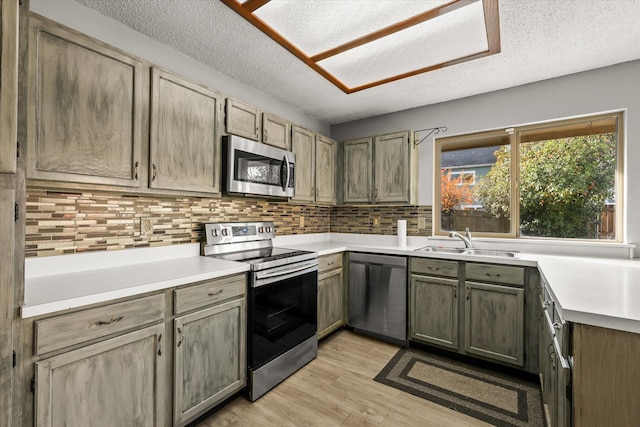 kitchen with sink, light hardwood / wood-style flooring, a textured ceiling, decorative backsplash, and appliances with stainless steel finishes