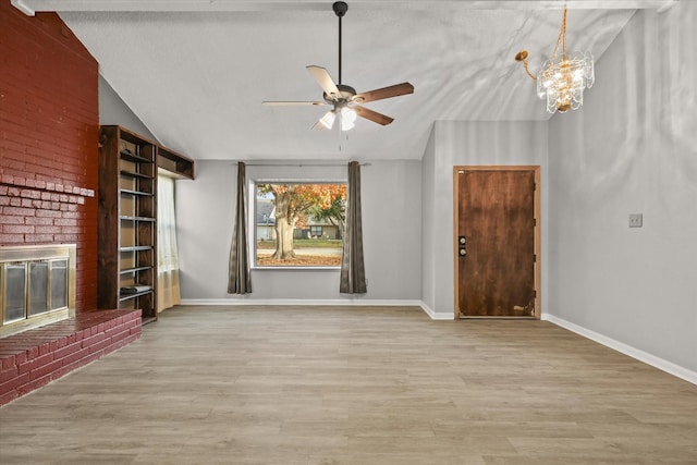 unfurnished living room with a brick fireplace, ceiling fan with notable chandelier, lofted ceiling, and light wood-type flooring